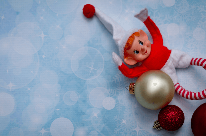 Lutin farceur rouge couché sur un décor d'hiver, à côté de boules de Noël