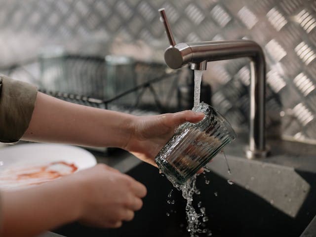 Personne rinçant un verre sous le jet d'eau d'un robinet