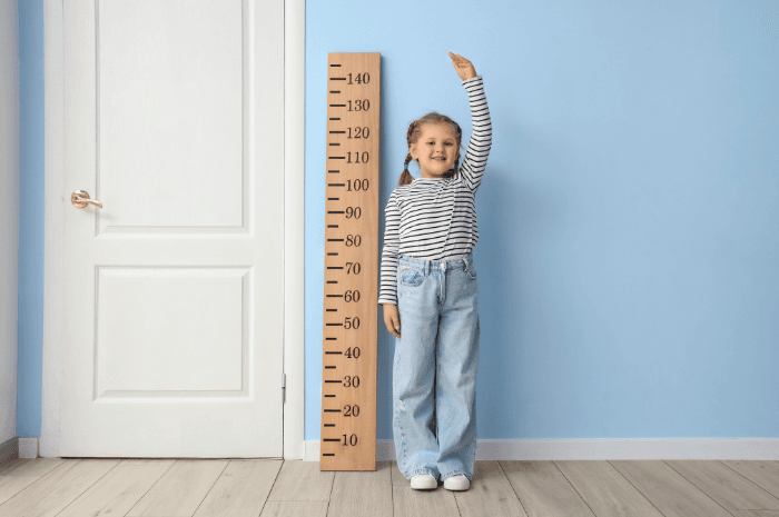Fille se mesurant à côté d'une échelle de croissance en bois