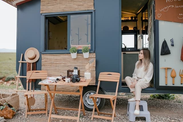 Femme assise dans l’entrée de sa mini maison sur roues