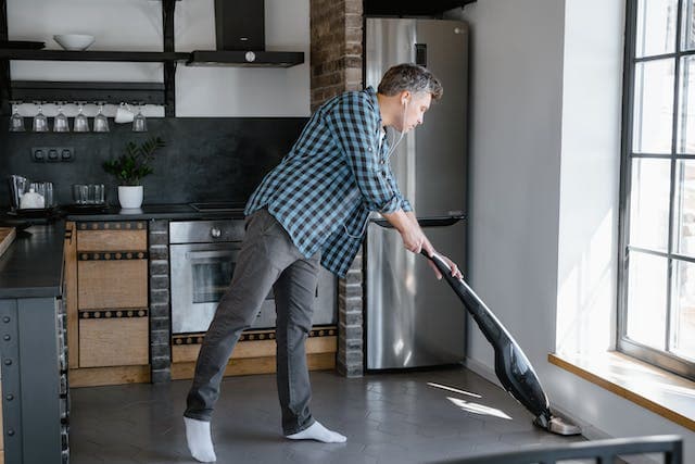 Homme passant la balayeuse dans sa cuisine