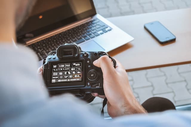 Homme réglant un appareil photo devant un ordinateur